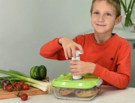 Dječak u kuhinji vakuumira vakuumsku posudu s ručnom vakuumskom pumpom.